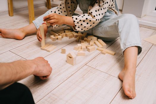 A little girl and her father build a tower out of wooden cubes. Playing with my father. Family game on the floor in the children's room.