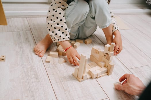Girl sits on the floor in a room and plays with her dad in a natral wood constructor. Playing with father. Happy Father's Day. Toys made of eco-friendly material.