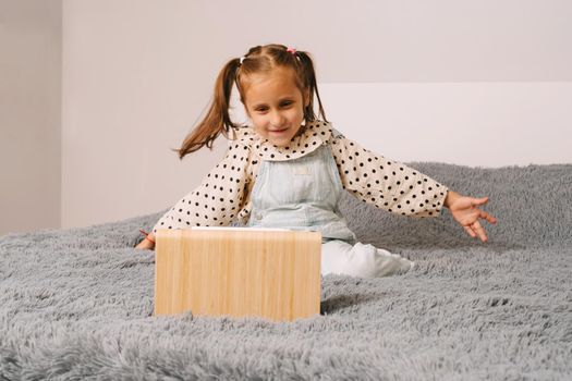 A little girl is talking very emotionally over a video link. The girl sits on the bed and watches cartoons or lessons. Distance learning via video communication.