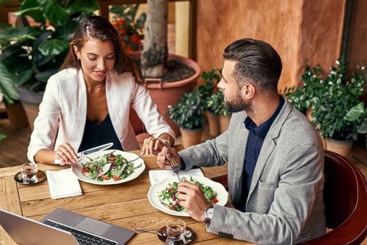 Business lunch. Man and woman sitting at table at restaurant eating healthy fresh salad talking smiling cheerful top view