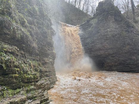 Beautiful landscape of powerful muddy waterfall in mountainous terrain. Dirty mountain waterway flows down and splashes