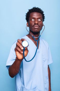 Goofy nurse holding stethoscope while rolling eyes. Healthcare specialist feeling playful while having medical instrument for heartbeat measurement in hand over isolated background.