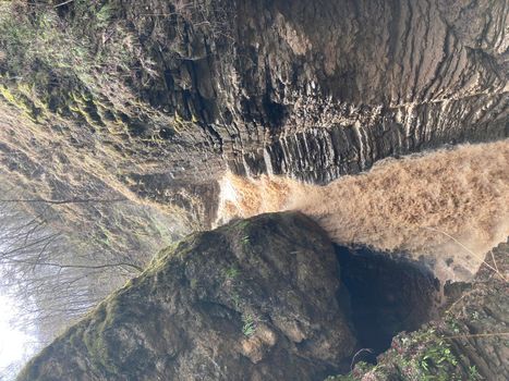 Beautiful landscape of powerful muddy waterfall in mountainous terrain. Dirty mountain waterway flows down and splashes