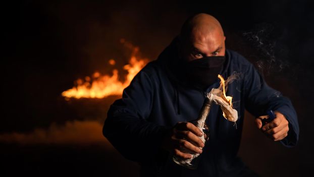A masked man is holding a burning bottle. Molotov cocktail