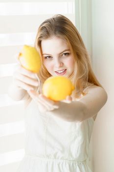 beautiful young woman in a white dress holds out two lemons and smiles. healthy lifestyle concept.