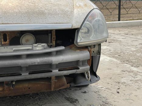 Close up of broken rusty car on city street. Damaged bumper of car after accident. Concept of careless driving