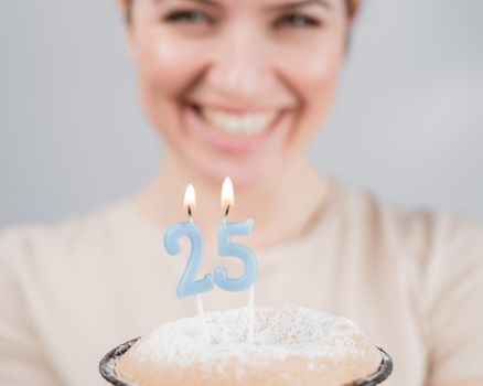 The happy woman makes a wish and blows out the candles on the 25th birthday cake. Girl celebrating birthday
