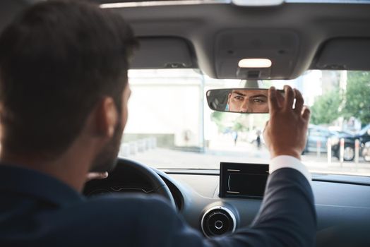 Partial view of handsome bisnessman behind the wheel adjusting rear view mirror.