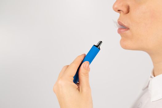 Caucasian woman smokes disposable vape on white background. Alternative device for smoking