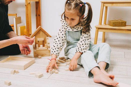 A little girl and her father build a tower out of wooden cubes. Playing with my father.