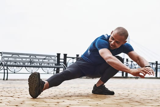 A close-up portrait of an african fitness man stretching legs on a quay background at the park. Side view