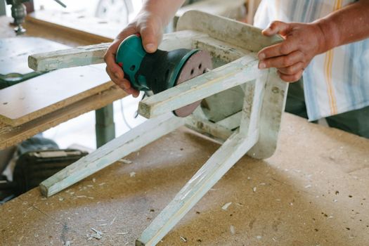 A man is polishing a white old stool. Grinding machine. Restoration of furniture.