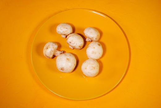 Close up of mushrooms on yellow plate. Raw white mushrooms on yellow background
