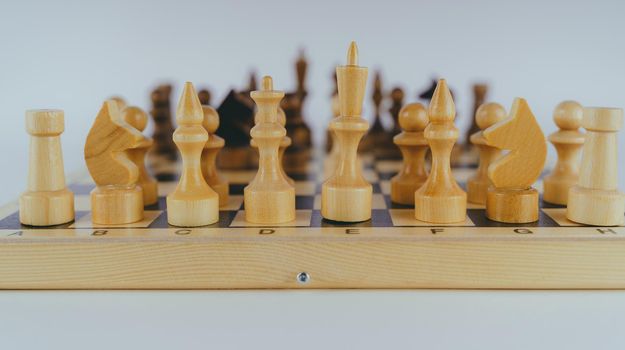 White and black wooden pieces on a chessboard. A chessboard set up during a game on a white background