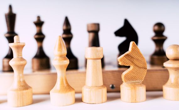 White and black wooden pieces on a chessboard. A chessboard set up during a game on a gray background