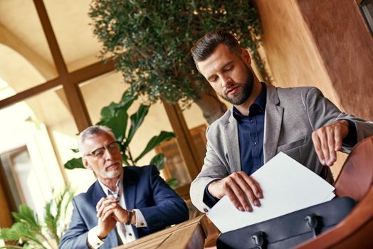 Business lunch. Two business people in the restaurant sitting at table one man taking contract from case serious. Team work concept