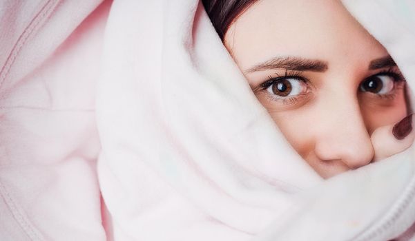 A woman looks out from under the blanket. Female hiding under a blanket
