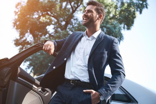 A young handsome man in a suit comes out of the car and laughs