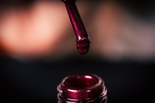 Close up of nail polish on blurry background. Maroon brilliant lacquer for manicure