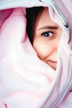 Portrait of young woman looking out of hoodie. Close up of pretty female hiding in sweatshirt and peeking out