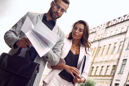 Preparing for meeting. Two young business people walking outside on the city street reading through documents concentrated bottom view close-up