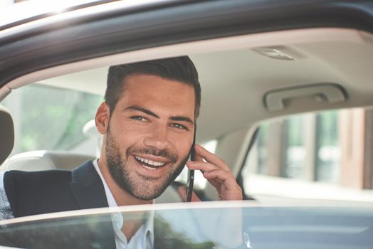 Young perfectionist. Handsome young man in full suit looking at his smart phone while sitting in the car