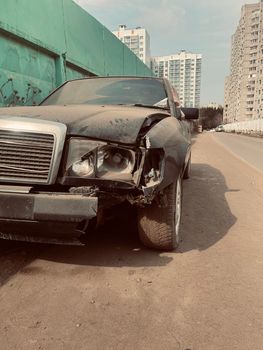 Close up of broken car on side of road. Damaged bumper, headlight and bodywork of black car after accident. Concept of careless driving.