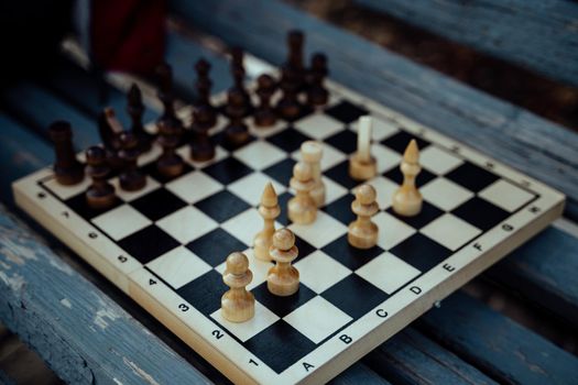 Close up of chess on wooden bench. Body part of unrecognizable woman playing in board game in city park