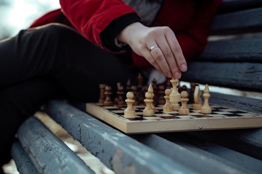 Close up of chess on wooden bench. Body part of unrecognizable woman playing in board game in city park