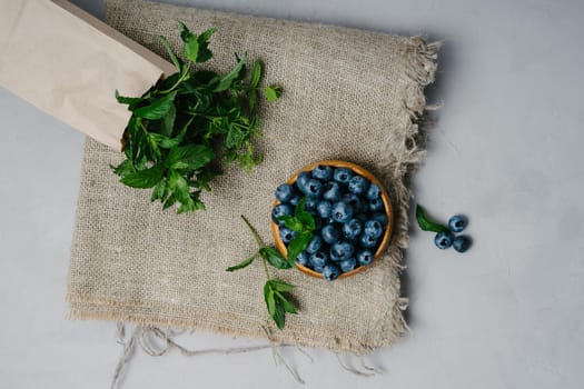 A small wooden bowl with berries. Juicy and ripe blueberries in an eco-friendly dish. Sprigs of fresh mint in a kraft bag. The concept of healthy eating and nutrition