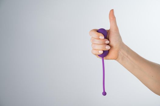 A woman recommends an electronic Kegel trainer for training pelvic floor muscles on a white background. Thumb up.