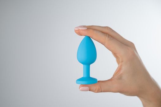 Woman holding a blue anal plug on a white background. Adult toy for alternative sex.