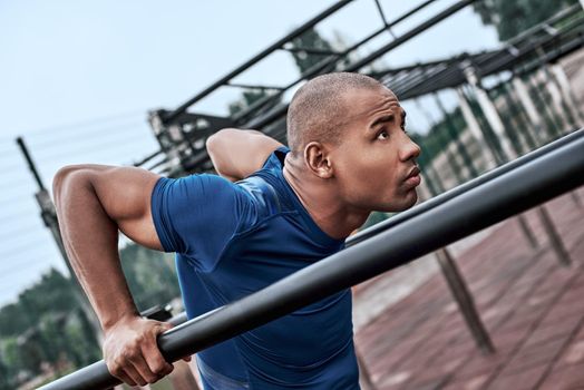 An african man is exercising at open air gym. Close-up photo of black african handsome guy in sports clothes is doing exercises for his hands