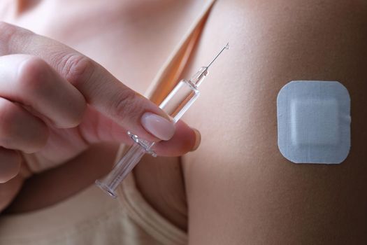 A woman holds a syringe with a medication, close-up. Beauty injections, plaster on the arm. Virus vaccine