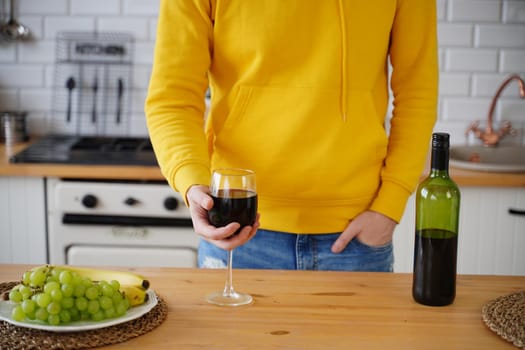 Close up of unrecognizable man with glass of red wine. Body part of unknown guy with alcohol in kitchen