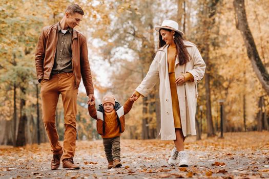 Father and mother with son walking in the autumn Park. A family walks in the Golden autumn in a nature Park