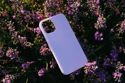 Silicone check for a smartphone lies on a lavender bush. Natural background. Lavender cultural field. Protective phone case lilac color.