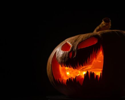 A creepy pumpkin with a carved grimace glows. Jack on a lantern in the dark