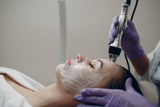 Young woman receiving electric RF lifting facial massage at beauty spa with electroporation equipment in clinic