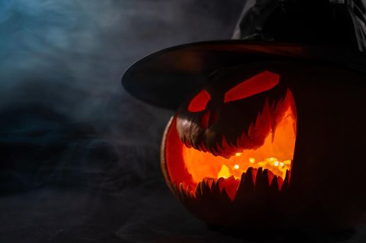 A creepy pumpkin with a carved grimace in the smoke. Jack o lantern in the dark