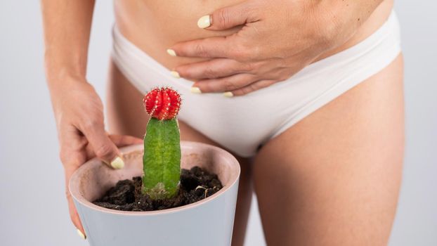 Woman in white panties holds a cactus with hand on her stomach