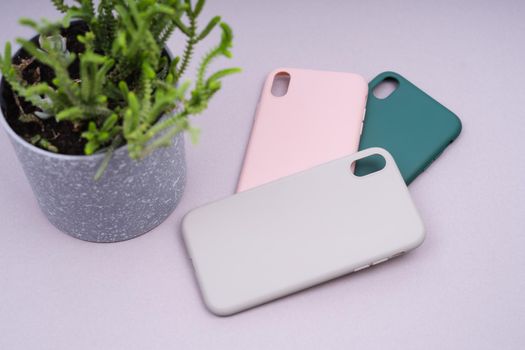 A few silicone cases for the smartphone. Grey, green and pink smartphone cases. Protect your phone. Green plant in a gray pot.