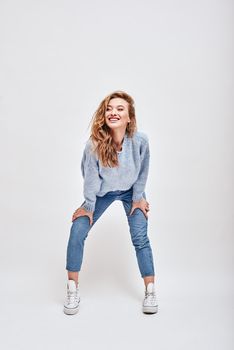 Portrait of young beautiful girl with brown hair wearing blue sweater, jeans and converse, smiling, while looking aside isolated over white background