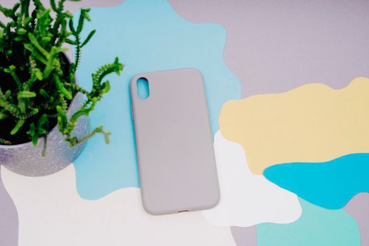 Protective covers for the smartphone. The gray silicone case for the smartphone lies on an abstract background. background of gray, yellow, white, green and blue. Pot with a house plant.