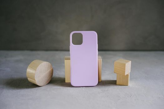 Lilac silicone case for smartphone on a gray textured background. Wooden three-dimensional figures of small size.