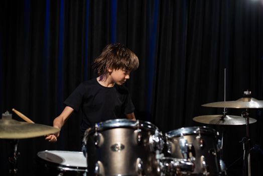 The boy learns to play the drums in the studio on a black background. Music school student.