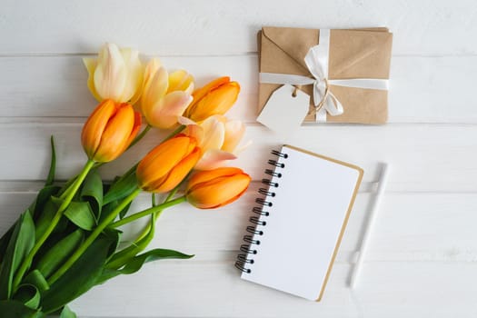 A notebook with a clean white sheet, a bouquet of beautiful flowers, craft ingess bandaged with white satin ribbon, a handle lie on a white wooden table. Flat lay.