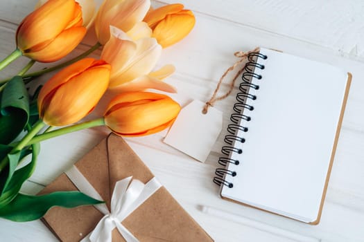 A notebook with a clean white sheet, a bouquet of beautiful flowers, craft ingess bandaged with white satin ribbon, a handle lie on a white wooden table. Flat lay.