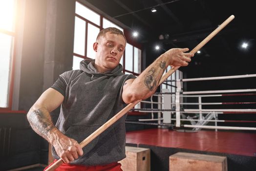 Focused young muscular athlete in colored sports clothing warming up his muscles before training in black boxing gym