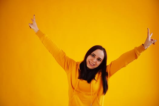 Portrait of young woman on yellow background. Pretty brunette in yellow hoodie posing on bright background